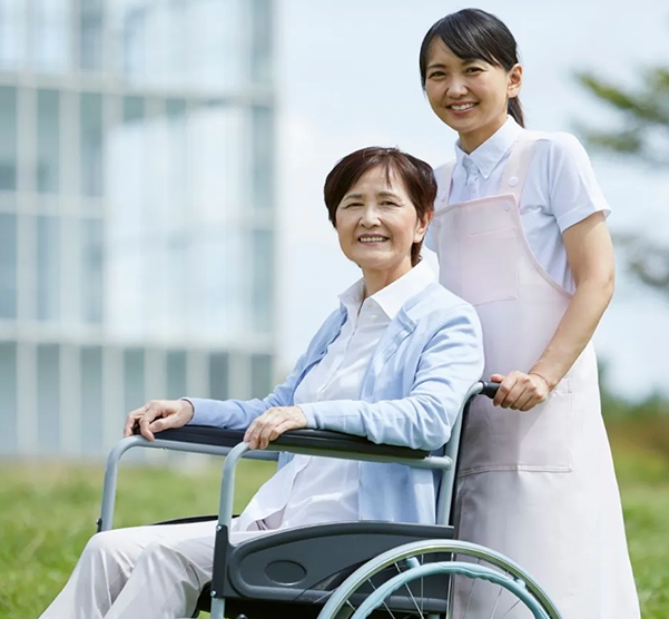 Caregiver pushing elderly woman in wheelchair outdoors.