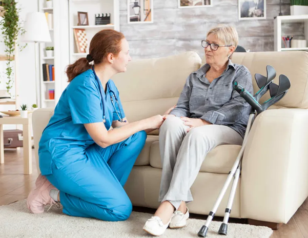 Nurse kneeling, talking to an elderly woman on a couch.